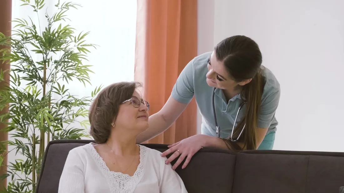 ممرضة تتحدث مع سيدة مسنة في غرفة معيشتها